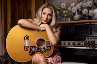 a woman is posing with an acoustic guitar in front of a piano