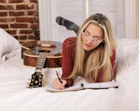 a woman laying on a bed with a guitar and a notebook